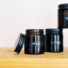 Load image into Gallery viewer, Set Of 7 Mini Amber Glass Jars With Black Lids And Stamped Labels
